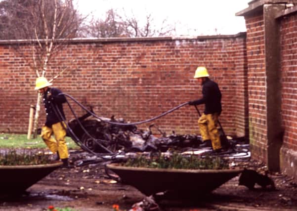 Firefighters pictured beside the barely-recognisible shell of a car, which housed a bomb that was placed deliberately at the gates of Roselawn cemetery / crematorium to disrupt an RUC funeral
