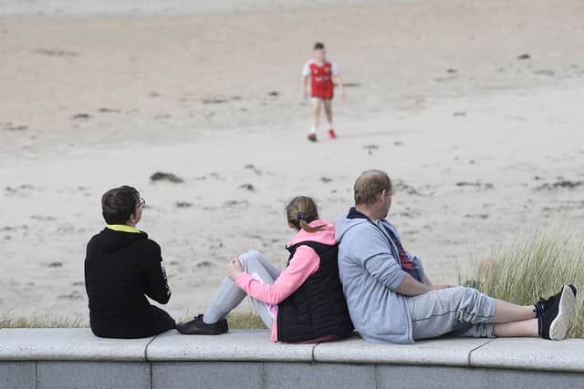 People sit on the sea wall of Castlerock Beach during the bank holiday weekend. Picture: Michael Cooper