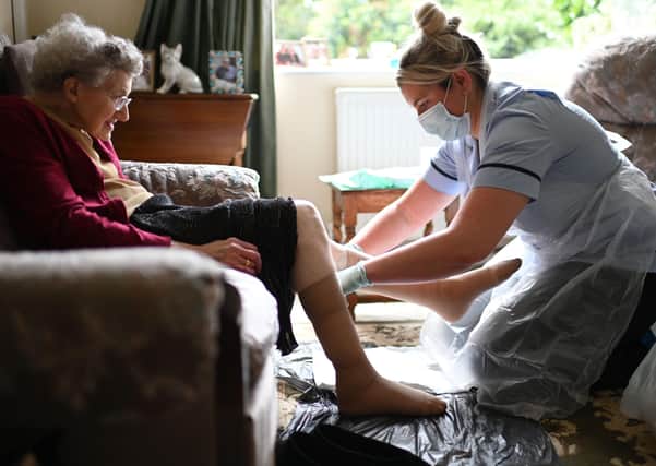 A nurse  wearing personal protective equipment (PPE), changes the dressings on the legs of an elderly woman.