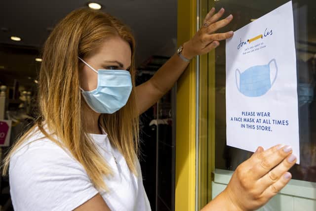 Joanne Millar store manger of Joules in Belfast places a sign in the shop window advising customers that face masks must be worn at all times as face coverings are now compulsory for shoppers in Northern Ireland.