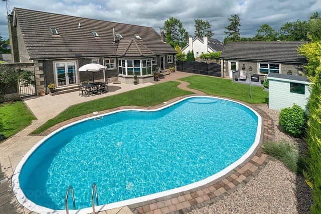 The rear of the property in a mix of lawn and decorative stone and paving around the outdoor heated swimming pool
