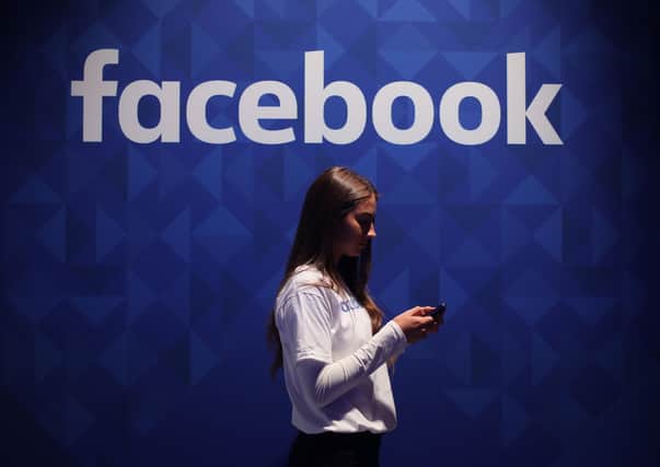 A woman using her phone under a logo of the social media giant Facebook; the PSNI wants bodies like Facebook to be forced to take down 'offensive' things