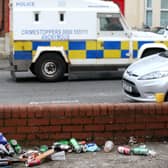 A police patrol drives past a host of discarded beer tins and bottles in a front garden of a Holylands house on Wednesday