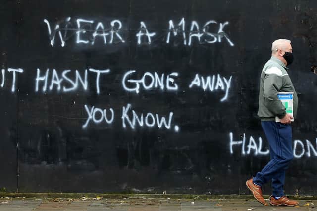 A man walks past graffiti on a wall in Belfast yesterday urging people to wear face masks