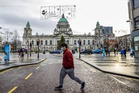 A man wearing a mask walks along Donegall Place in front of Belfast City Hall.