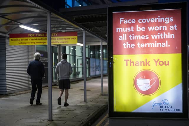 Two men walk passed a sign that face coverings must be worn at all times within the terminal at George Best Belfast City Airport.