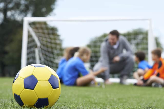 Coach And Team Discussing Soccer Tactics With Ball In Foreground
