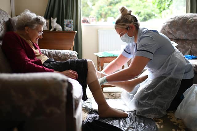 A nurse in PPE changes the dressings on an old woman’s legs
