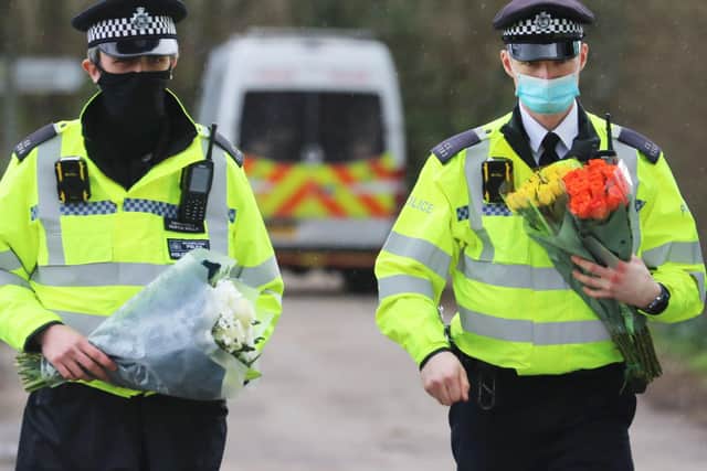 Police officers carry flowers from members of the public at Great Chart Golf and Leisure near Ashford in Kent following the discovery of human remains in the hunt for missing Sarah Everard.