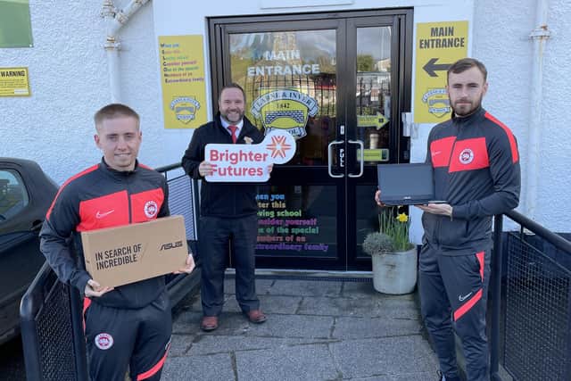 Larne players Conor McKendry (left) and Luke Wade Slater present the first laptop donations to Kirk Patterson, principal of Larne and Inver Primary School.