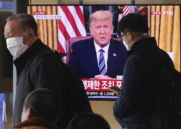Masked people walk in front of a TV screen showing a live broadcast of U.S. President Donald Trump's speech at the Seoul Railway Station in Seoul, South Korea, Thursday, March 12, 2020