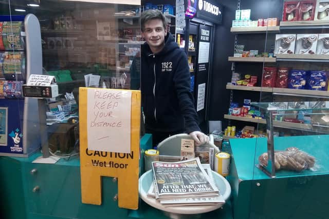 Jack McKinnell, an A Level student who is now out of school due to coronavirus, serving at Mace Brunswick in Bangor West, behind a counter with protective screens and a sign to keep distance, on Saturday evening March 21 2020