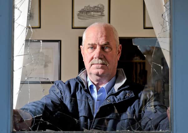 Ken Wilkinson stares through a shattered window at his home after a pipe bomb attack in 2010
