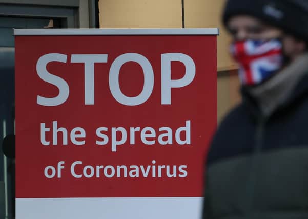 A man wearing a face mask walks past a coronavirus advice sign . Photo credit: Andrew Milligan/PA Wire