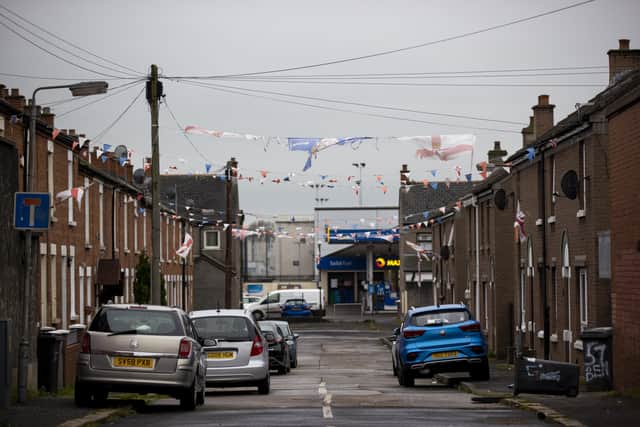 Tattered Northern Ireland Centenary flag and St George’s flags with bunting flies between homes in the loyalist area of The Village in south Belfast. Picture date: Tuesday November 30 2021.