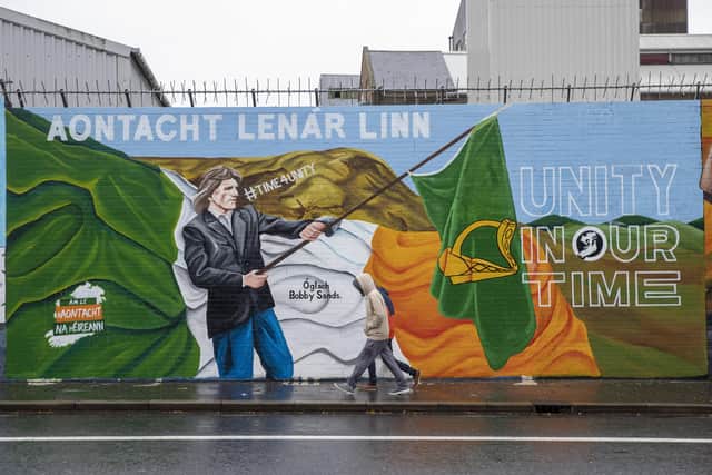 Two people walk past a Sinn Fein mural painted on International Wall in Belfast showing a depiction of irish republican Bobby Sands with the message, Unity In Our Time. Picture date: Tuesday November 30 2021.