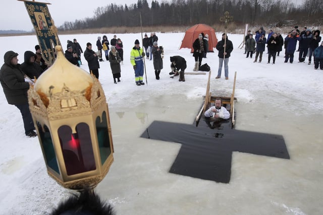 A Russian Orthodox priest conducts a service in the icy water on Epiphany at a hole in the form of Orthodox Cross at a lake in Orlino village, 70 kilometers (43 miles) south of St Petersburg, Russia in January 2018. Thousands of Russian Orthodox Church followers plunged into icy rivers and ponds across the country to mark Epiphany, cleansing themselves with water deemed holy for the day. (AP Photo/Dmitri Lovetsky)