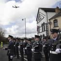 An RAF Poseidon maritime patrol aircraft in the background as uniformed personnel pause for reflection at the Limavady War Memorial