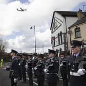 An RAF Poseidon maritime patrol aircraft in the background as uniformed personnel pause for reflection at the Limavady War Memorial
