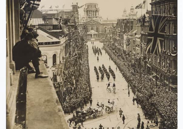 View from top floor window of building on corner of Castle Place and Royal Avenue showing crowds watching the Royal Procession approaching the City Hall for the state opening of the first Northern Ireland Parliament 22 June 1921, with people sitting on window ledge. Catalogue number:BELUM.Y22657. Robert John Welch, (1859-1936), © National Museums NI, Collection Ulster Museum