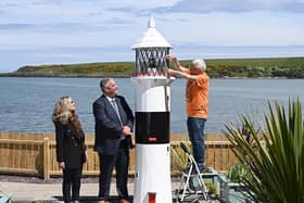 A ten-foot-tall lighthouse built by prisoners in Maghaberry will help shine a spotlight on the convalescent work of the cancer charity Hope House. The wooden structure, which took several months to construct in Maghaberry Prison, was this week relocated to Hope House Cottage on the beach at Browns Bay, Islandmagee.
Looking on as charity volunteer Sam McCullough makes a final adjustment to the lighthouse, are David Savage, Governor Maghaberry Prison and Dawn McConnell, Founder of the Hope House charity. Picture: Michael Cooper