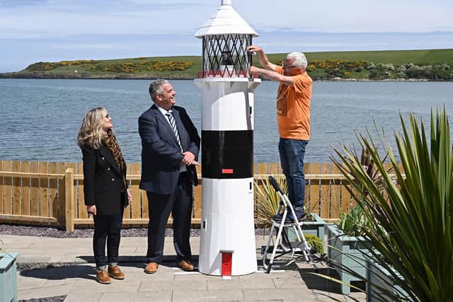 A ten-foot-tall lighthouse built by prisoners in Maghaberry will help shine a spotlight on the convalescent work of the cancer charity Hope House. The wooden structure, which took several months to construct in Maghaberry Prison, was this week relocated to Hope House Cottage on the beach at Browns Bay, Islandmagee.
Looking on as charity volunteer Sam McCullough makes a final adjustment to the lighthouse, are David Savage, Governor Maghaberry Prison and Dawn McConnell, Founder of the Hope House charity. Picture: Michael Cooper