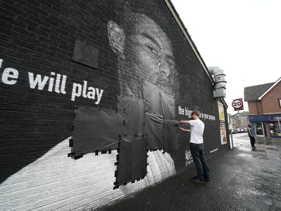 Ed Wellard, from Withington, tapes bin liners across offensive wording on the mural of Manchester United striker and England player Marcus Rashford on the wall of the Coffee House Cafe on Copson Street, Withington, which appeared vandalised the morning after the England football team lost the UEFA Euro 2021 final.