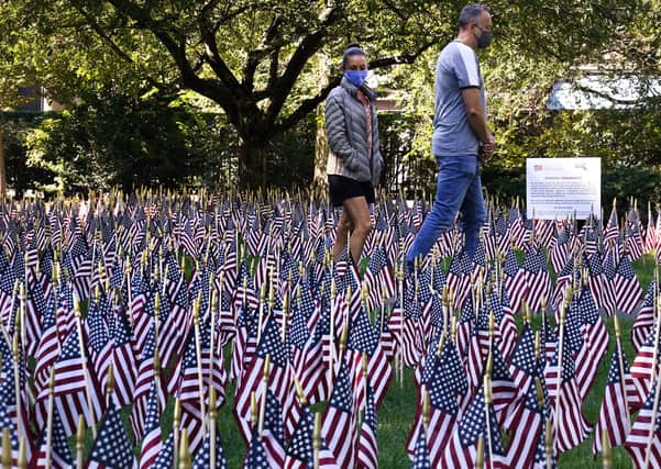 A couple, wearing protective masks due to the COVID-19 virus outbreak, walk along a path through nearly 3,000 flags, each representing a victim lost on September 11, 2001 in the attack on the World Trade Center, at the Public Garden, Friday, Sept. 10, 2021, in Boston. (AP Photo/Charles Krupa)