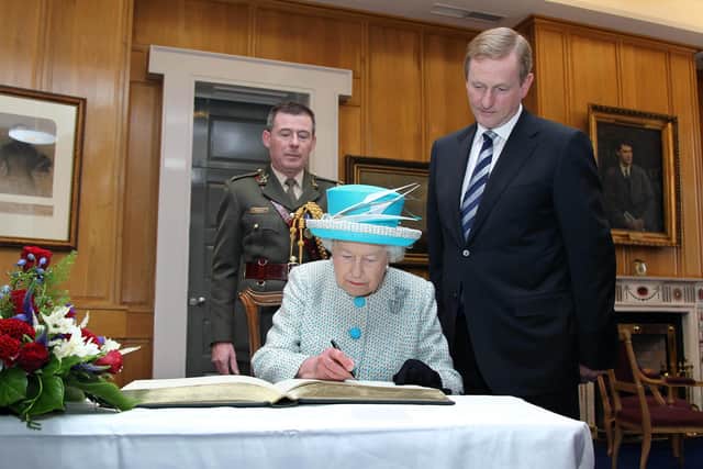 Queen Elizabeth II signing the visitors' book, as Taoiseach Enda Kenny looks on, at Government Buildings, Dublin, during the second day of her State Visit to Ireland.