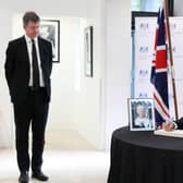 Taoiseach Micheal Martin signing a book of condolences for Queen Elizabeth II in the British Embassy, Dublin, as Paul Johnston, British Ambassador to Ireland, looks on.