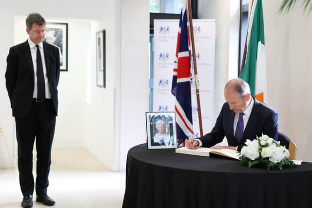 Taoiseach Micheal Martin signing a book of condolences for Queen Elizabeth II in the British Embassy, Dublin, as Paul Johnston, British Ambassador to Ireland, looks on.