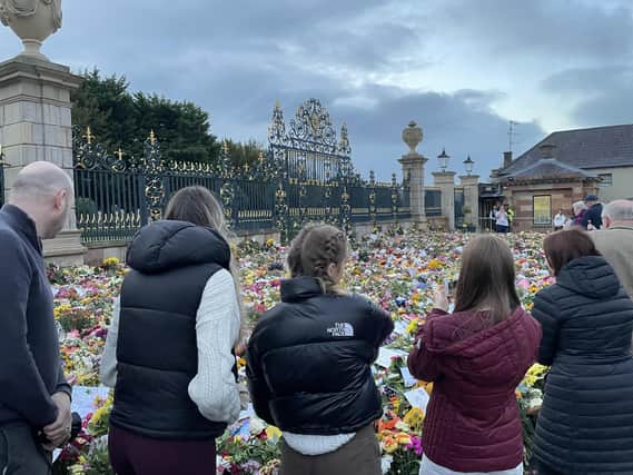 People look at the hundreds of floral  tributes left at the gates of Hillsborough Castle before Sunday's minute's silence