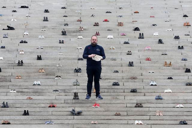 Independent Belfast City Councillor Paul McCusker on the steps of Stormont surrounded by more than 200 pairs of shoes which have been laid to show the number of people who have died in Northern Ireland following a drug addiction