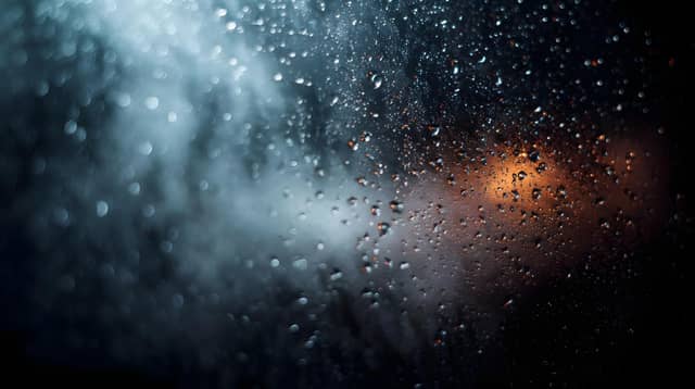 Detailed close up of water condensation forming numerous clear droplets on a dark wet glass window pane