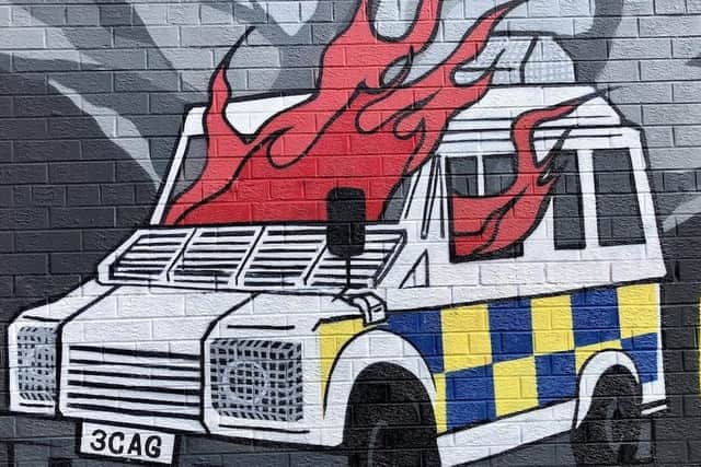 A mural of a burning police van, unveiled by Kneecap in 2022. Other motifs the band uses on its merchandise are petrol bombs and balaclavas