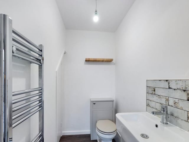 Here is the downstairs toilet or guest WC. It comprises a low-flush WC and wash hand basin with vanity unit, mixer tap and splashback tiling. Not to mention a laminate wood-effect floor and a chrome ladder-style central heating radiator/towel rail
