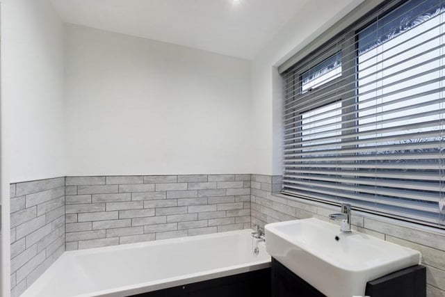 The bathroom also includes this panelled bath with hot and cold mixer tap, plus wood-effect laminate flooring, inset ceiling spotlights, an extractor fan and a chrome ladder-style central heating radiator/towel rail.