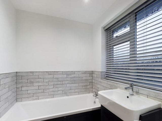 The bathroom also includes this panelled bath with hot and cold mixer tap, plus wood-effect laminate flooring, inset ceiling spotlights, an extractor fan and a chrome ladder-style central heating radiator/towel rail.