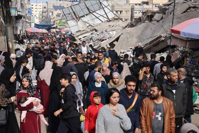 Crowds of people walk past destroyed buildings in the southern Gaza Strip city of Khan Yunis on November 28, 2023. In Khan Yunis, where the population nearly doubled following the arrival of the displaced from the northern Gaza Strip, war-weary Palestinians remain sceptical about the Israel-Hamas deal to exchange hostages for prisoners. (Photo by MOHAMMED ABED / AFP) (Photo by MOHAMMED ABED/AFP via Getty Images)