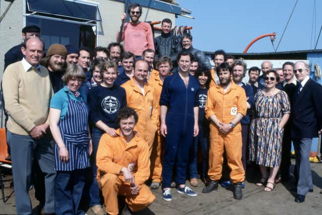 April 1982. Fresh from a dive, the then HRH The Prince of Wales (centre front) together with Margaret Rule and Wendell Lewis (Director of Salvage and Recovery) (far right), members of the archaeological and salvage diving teams and the some of the ships crew. Alex Hildred (L) and Barrie Andrian (r) are wearing Mary Rose Diving Team sweatshirts.