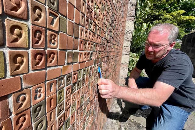 Mark Wylie of DC Tours cleans the Troubles memorial using a toothbrush. Pic: John Baucher