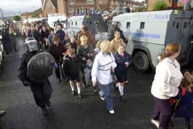 Children and parents make their way to the Catholic Holy Cross School, in the Prostestant area of Ardoyne in Belfast as loyalists make a silent protest on the other side of the Royal Ulster Constabulary vehicles.