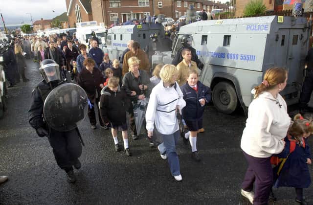 Children and parents make their way to the Catholic Holy Cross School, in the Prostestant area of Ardoyne in Belfast as loyalists make a silent protest on the other side of the Royal Ulster Constabulary vehicles.