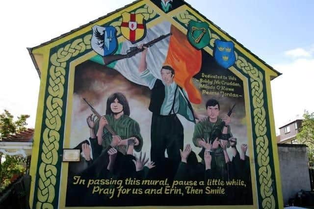 A mural glorifying three Provisional IRA members on Divismore Way, west Belfast; the mural stands next to a large stone memorial plaza dedicated to IRA members