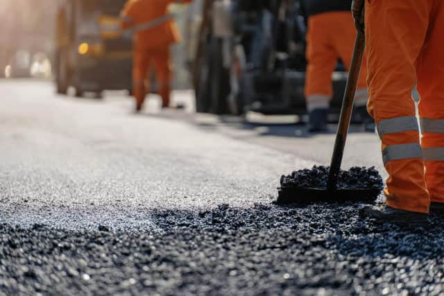 Road construction worker leveling fresh asphalt with rake during road construction and repair works