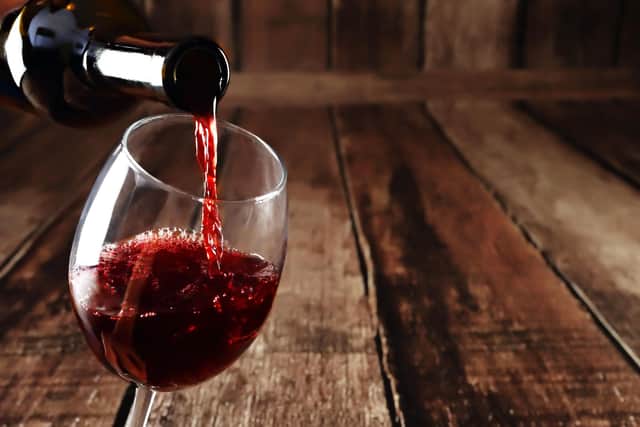 Red wine in glass on wooden background. Beautiful alcohol background. Red wine pouring from bottle. Free space for text on wooden backdrop.