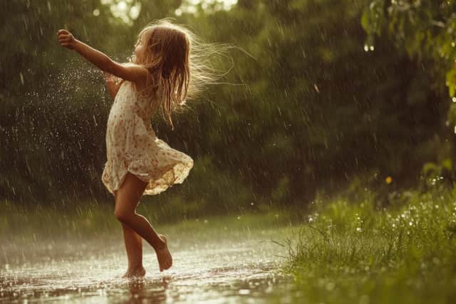 Happy girl dancing barefoot in rain puddle.
