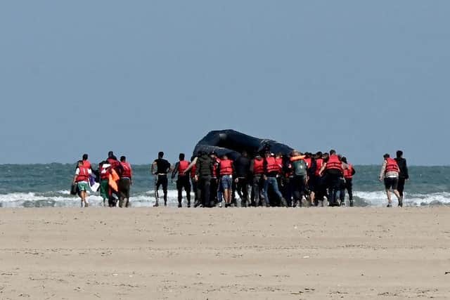 Migrants push an inflatable boat across a stretch of sand towards the water, near Gravelines, northern France, on August 25, 2022, before they attempt to cross the English Channel to Britain (Photo by DENIS CHARLET/AFP via Getty Images)