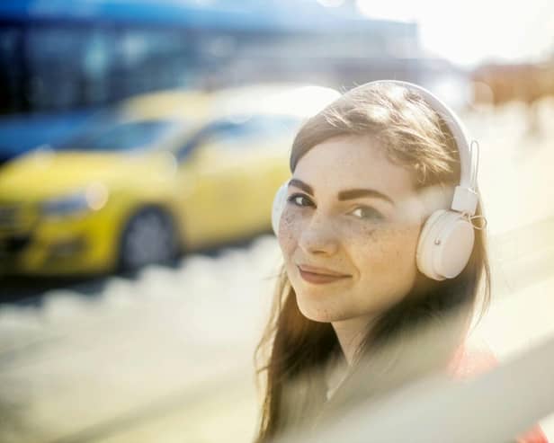 Young woman with freckles listens to music through white headphones, enjoying a sunny city vibe.
