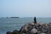 An Iranian woman stands overlooking the water as ships are seen anchored in the Strait of Hormuz on August 10, 2026 off the coast of Bandar Abbas, Iran (photo by Ali Saeedi/Getty Images)